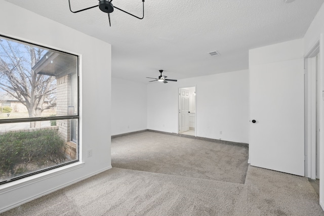 carpeted empty room featuring ceiling fan, visible vents, baseboards, and a textured ceiling