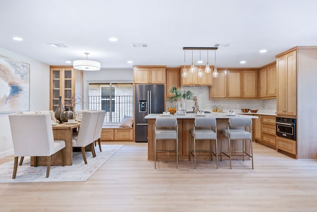 kitchen with a center island with sink, high end fridge, visible vents, light wood-style floors, and black oven