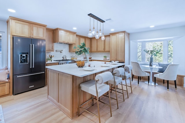 kitchen with high quality fridge, a kitchen island, visible vents, light brown cabinetry, and light wood finished floors