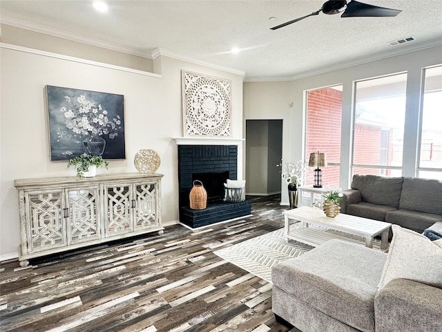 living room with a textured ceiling, wood finished floors, visible vents, ornamental molding, and a brick fireplace