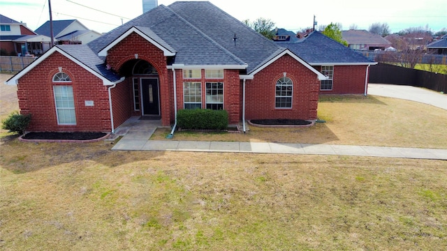 view of front of home featuring a shingled roof, fence, a front lawn, and brick siding