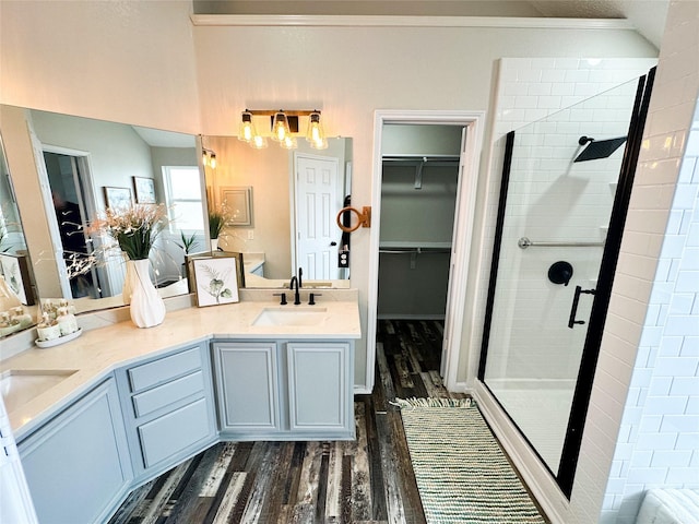 full bathroom featuring a stall shower, a walk in closet, a sink, and wood finished floors