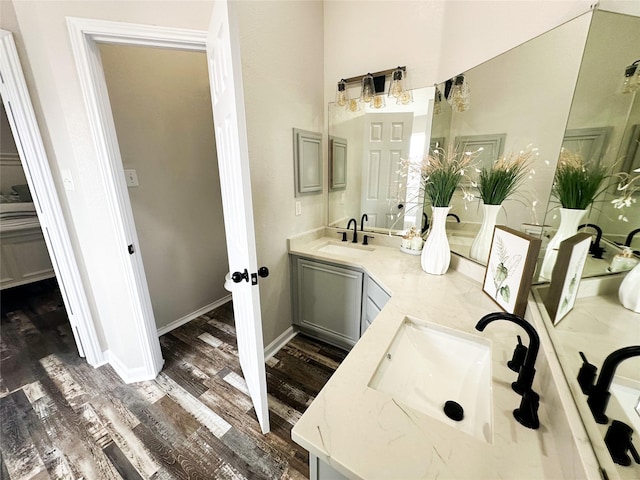 full bath featuring double vanity, baseboards, a sink, and wood finished floors