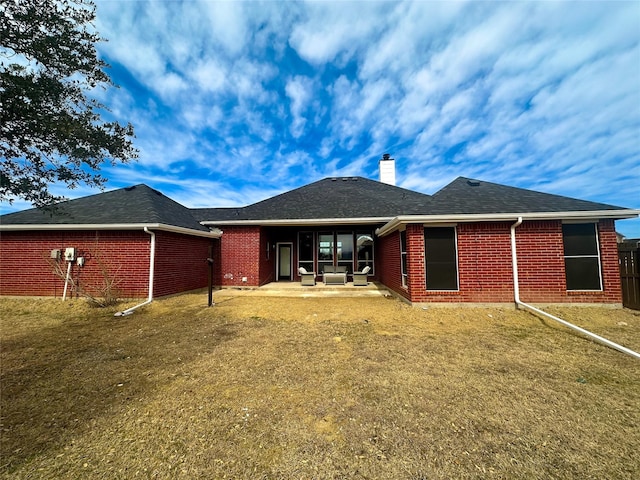 rear view of house with a shingled roof, brick siding, a patio, and a chimney