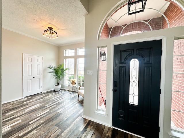 foyer featuring a textured ceiling, baseboards, wood finished floors, and crown molding