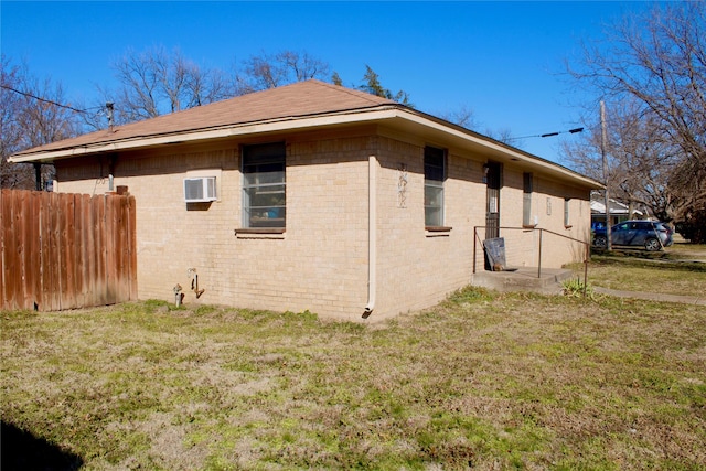 view of home's exterior featuring an AC wall unit, fence, a lawn, and brick siding