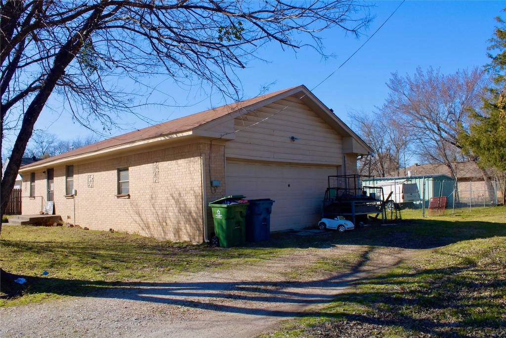 view of property exterior with brick siding, an outdoor structure, fence, a yard, and driveway