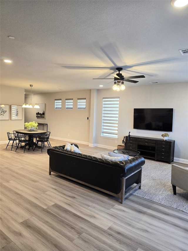 living room featuring a textured ceiling, light wood-style flooring, visible vents, and baseboards