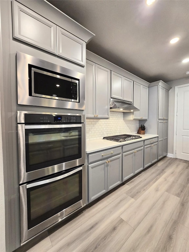 kitchen featuring tasteful backsplash, gray cabinetry, appliances with stainless steel finishes, light wood-type flooring, and under cabinet range hood