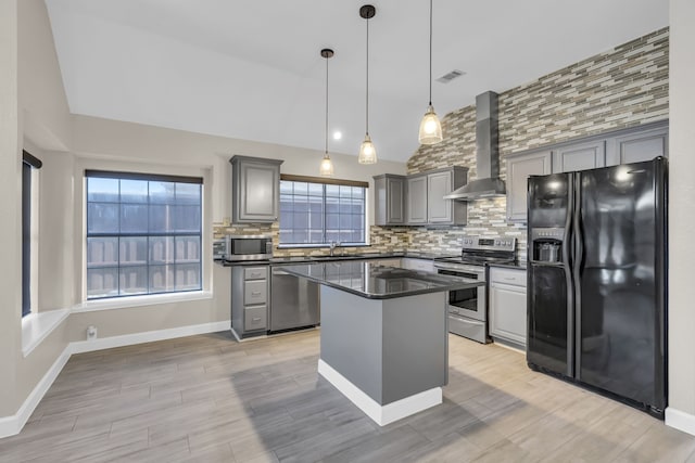 kitchen featuring gray cabinetry, stainless steel appliances, a sink, wall chimney range hood, and dark countertops