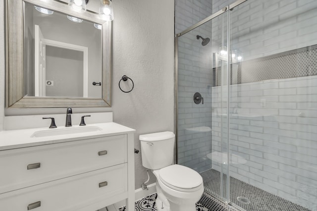 bathroom with a textured wall, a shower stall, toilet, and vanity