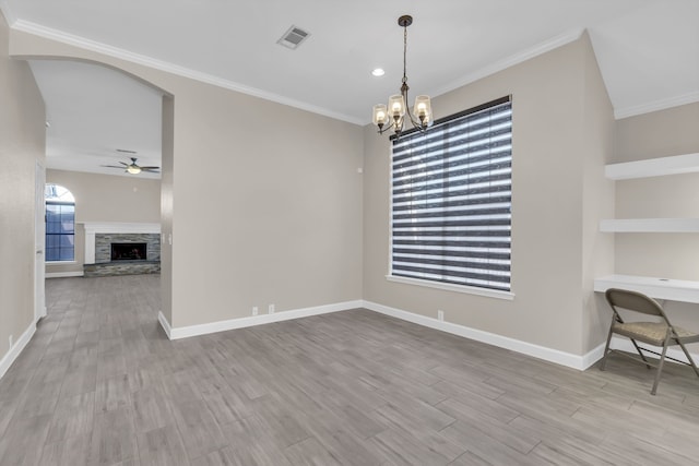 unfurnished dining area featuring baseboards, ceiling fan with notable chandelier, wood finished floors, and a stone fireplace