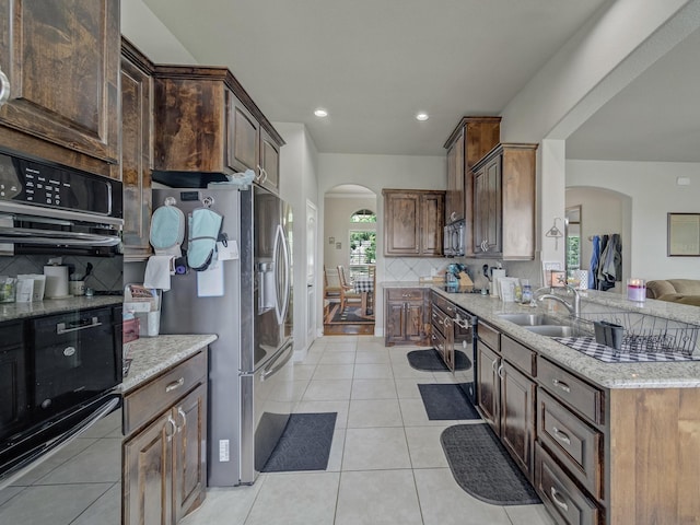 kitchen with arched walkways, stainless steel refrigerator with ice dispenser, light tile patterned floors, a sink, and black microwave