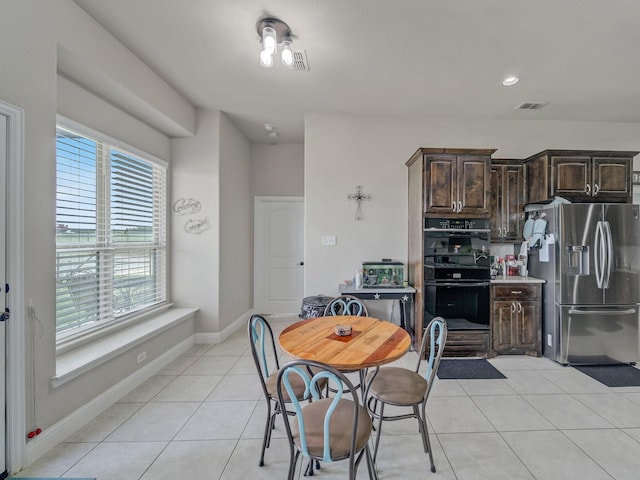 kitchen with light tile patterned floors, dobule oven black, visible vents, dark brown cabinetry, and stainless steel fridge with ice dispenser