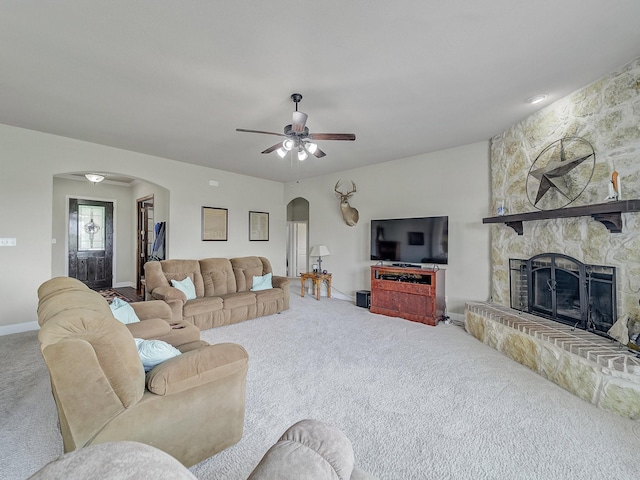 living area featuring carpet floors, arched walkways, a fireplace, a ceiling fan, and baseboards