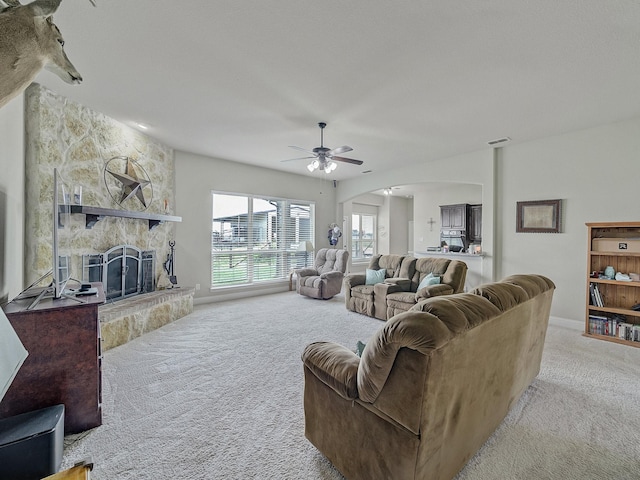 living area with arched walkways, carpet, visible vents, a ceiling fan, and a stone fireplace