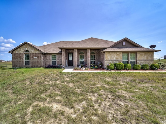 view of front of property featuring stone siding, roof with shingles, fence, a front yard, and brick siding