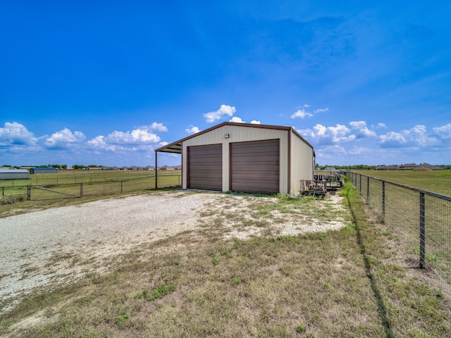 garage featuring driveway, a rural view, a detached garage, and fence