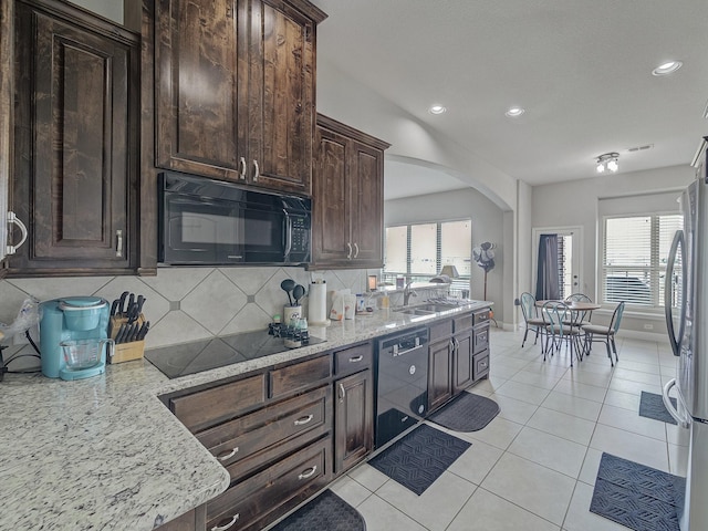 kitchen with arched walkways, light tile patterned floors, tasteful backsplash, a sink, and black appliances