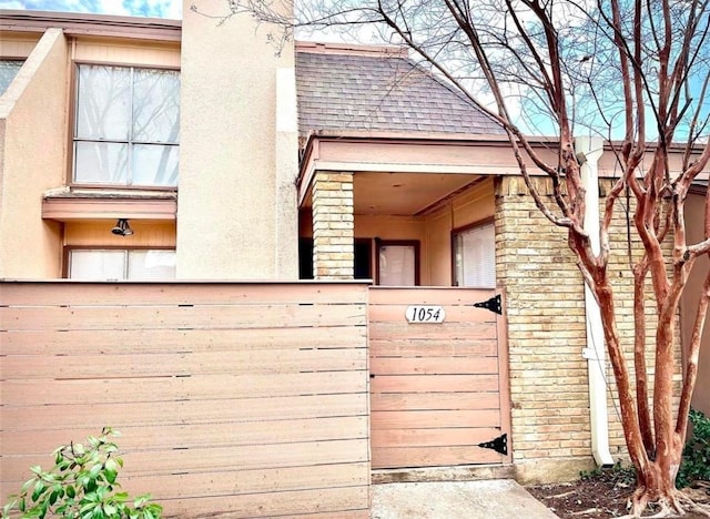 exterior space with a shingled roof, brick siding, and stucco siding