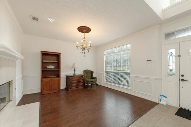 entrance foyer featuring a tiled fireplace, wood finished floors, visible vents, and a notable chandelier