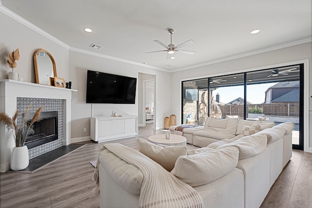 living room featuring a fireplace, visible vents, ornamental molding, ceiling fan, and wood finished floors