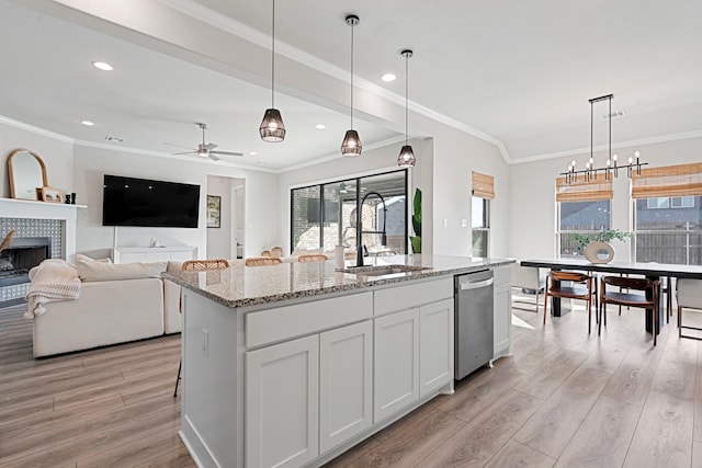 kitchen featuring dishwasher, light wood finished floors, a tile fireplace, and a sink