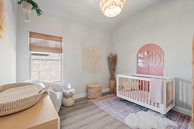 bedroom featuring lofted ceiling, wood finished floors, baseboards, a nursery area, and an inviting chandelier