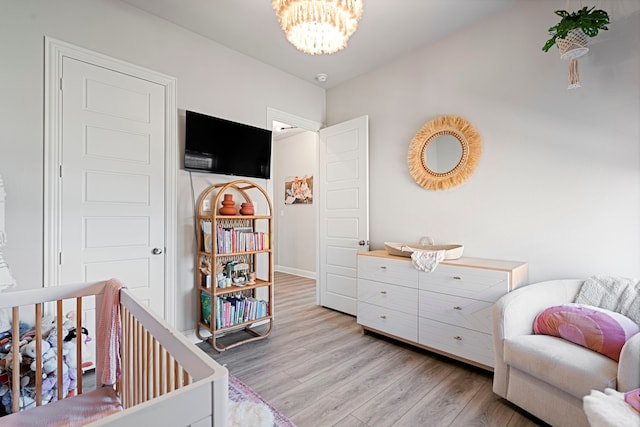 bedroom with a chandelier, a crib, baseboards, and light wood-style floors