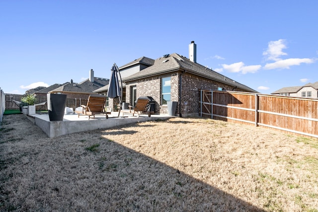 back of house featuring a yard, a patio, brick siding, and a fenced backyard