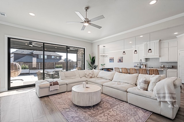 living area featuring visible vents, wood finished floors, ceiling fan with notable chandelier, crown molding, and recessed lighting