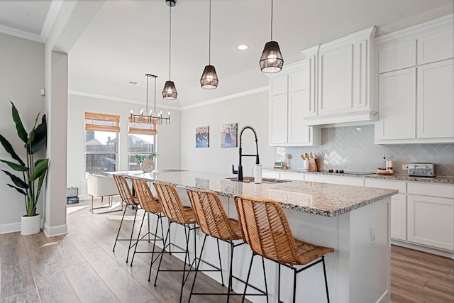 kitchen featuring crown molding, a sink, light wood finished floors, and decorative backsplash