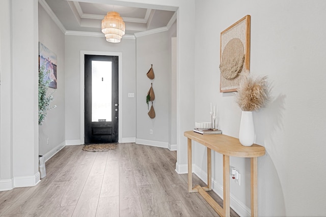 foyer featuring baseboards, light wood-style flooring, a tray ceiling, and crown molding