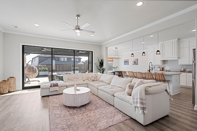 living room with ornamental molding, ceiling fan with notable chandelier, visible vents, and wood finished floors