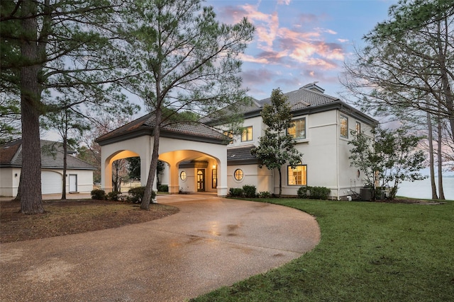 mediterranean / spanish-style house with an outbuilding, stucco siding, concrete driveway, a lawn, and a tiled roof