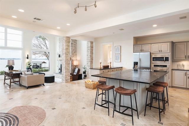 kitchen featuring visible vents, dark countertops, appliances with stainless steel finishes, a center island, and a kitchen bar