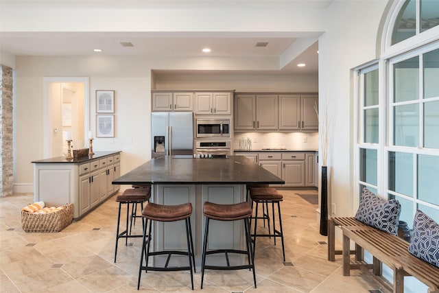 kitchen featuring stainless steel appliances, a kitchen bar, gray cabinetry, and tasteful backsplash