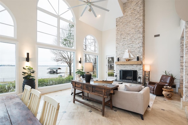 living area featuring light tile patterned floors, a fireplace, a towering ceiling, visible vents, and a ceiling fan