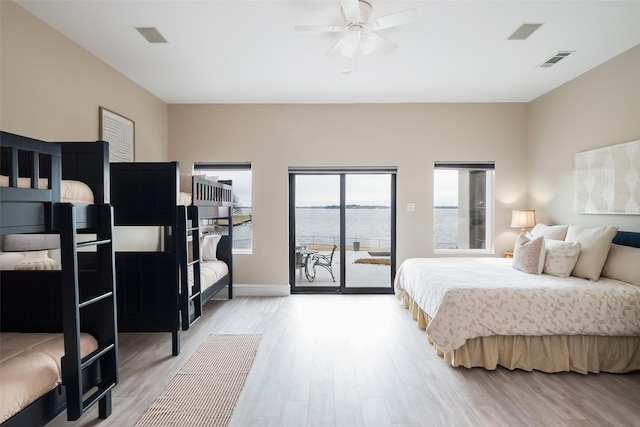 bedroom featuring light wood-type flooring, a water view, visible vents, and access to exterior