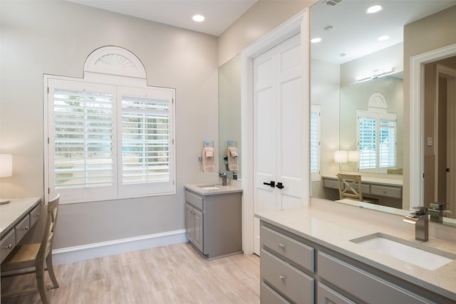 bathroom featuring wood finished floors, two vanities, a sink, and baseboards