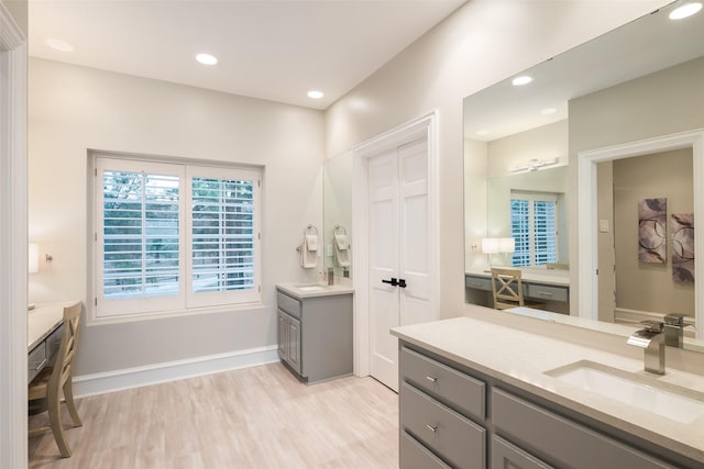 bathroom featuring recessed lighting, two vanities, a sink, wood finished floors, and baseboards