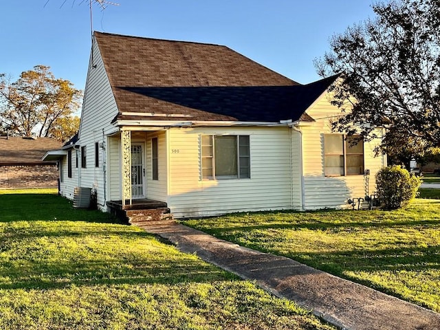 view of front of house with a front lawn, a shingled roof, and cooling unit