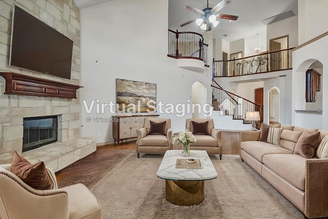 living room featuring arched walkways, a fireplace, a towering ceiling, wood finished floors, and stairs