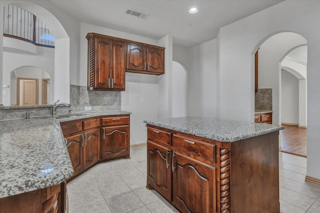 kitchen featuring light tile patterned floors, light stone countertops, a sink, visible vents, and decorative backsplash