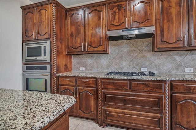 kitchen with light stone counters, light tile patterned floors, decorative backsplash, appliances with stainless steel finishes, and under cabinet range hood