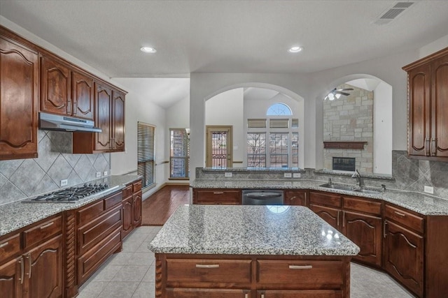 kitchen featuring light stone counters, under cabinet range hood, stainless steel appliances, a sink, and a center island