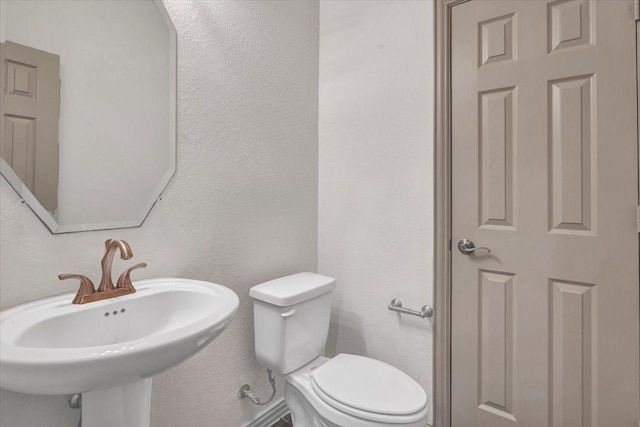 bathroom featuring toilet, a sink, and a textured wall