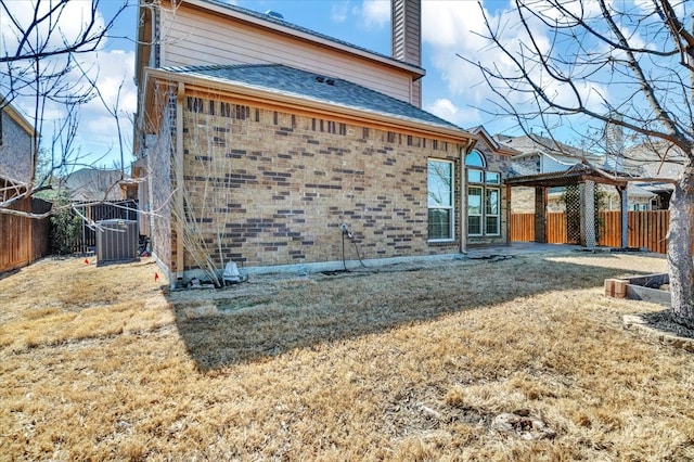 rear view of property featuring cooling unit, brick siding, fence, and a chimney