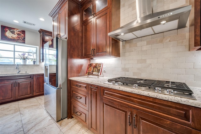 kitchen featuring light stone counters, visible vents, appliances with stainless steel finishes, a sink, and wall chimney range hood