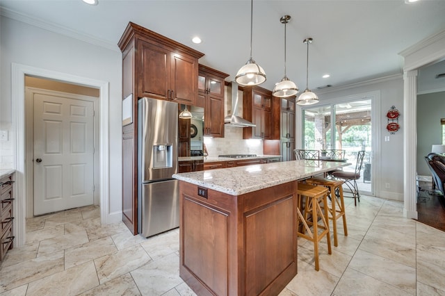 kitchen with wall chimney exhaust hood, ornamental molding, a kitchen island, and stainless steel appliances